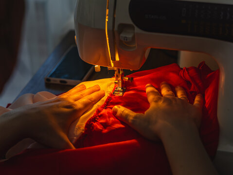 Hands sew fabric with sewing machine in evening light