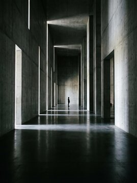 Solitary Figure in Monumental Concrete Hall with Light Beams