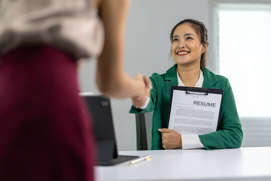 Happy businesswoman shaking hands with female applicant holding a resume during a job interview in office, recruitment process and professional opportunity.