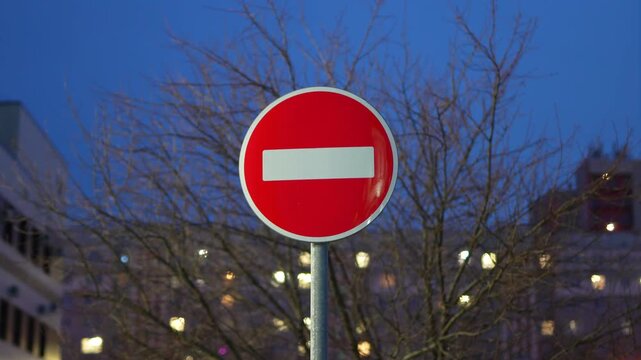 Red no entry sign against twilight sky with bokeh lights
