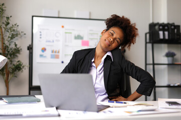 Naklejka premium Businesswoman experiencing neck and back pain while working on a laptop in the office, stretching her neck and closing her eyes to relieve tension and discomfort.