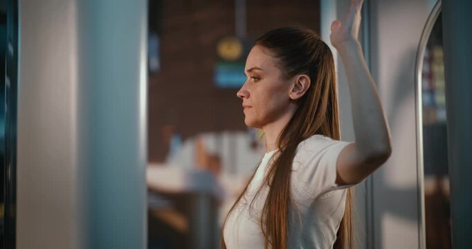 Female Traveler in High Tech Millimeter Wave Scanner at Departure Hall. Woman in White T Shirt Standing in Luminous Scanning Arch. Safety, Technology, Systematic Approach to International Air Travel.