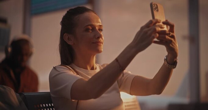 Sitting With Suitcase Near, Woman Engages in Video Call During Layover. Female Looks Into Phone Camera, Laughing and Chatting. Connected Traveler Lifestyle. Mobile Communications, 5G Connectivity.