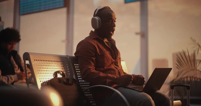 Sitting in Departure Lounge, Black Professional Engages in Business Video Call on Laptop. Man Wears Headphones For Clear Audio, Speaking Confidently While Warm Golden Hour Light Fills Terminal.