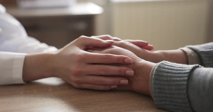 Female doctor gently holding hands of woman patient during close conversation about health concerns, diagnosis, or treatment. Healthcare, reassurance, understanding, emotional support in medical care