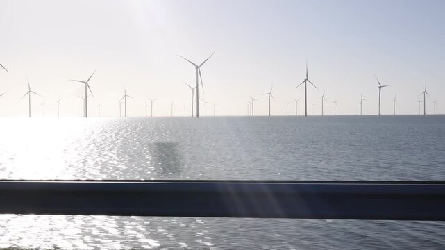 Moving side view with a foreground barrier and distant wind turbines in warm early light.