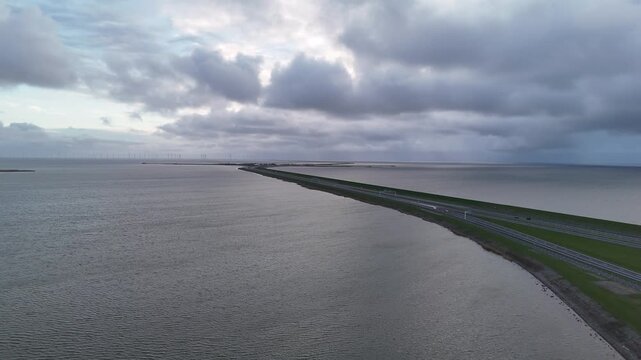 High aerial view of the Afsluitdijk approach at dusk with cloudy sky and the first dam structures visible.