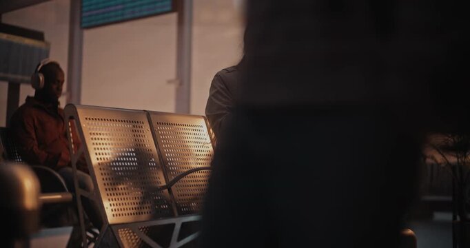 Stylish Woman Wearing Classic Beige Trench Arrives at Departure Terminal With Suitcase. Seat on Bench in Front Large Panoramic Windows, Bathed in Glow Setting Sun, Uses Smartphone Scan Boarding Pass.