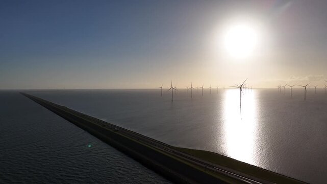 High aerial view from above the sea showing the curving dyke and the offshore turbines together.