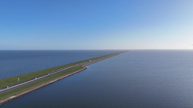 Oblique aerial view from Breezanddijk showing the vast length of the Afsluitdijk cutting across water under morning light.