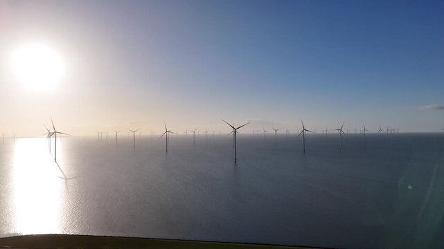 Forward aerial approach with tiny passing cars below and glowing turbines ahead in warm light.