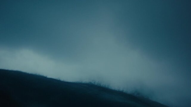 Dark stormy ocean surface under heavy cloudy sky as wave lip crashes forward with mist obscuring air, slow motion