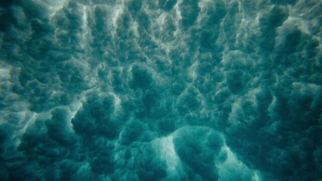 Underwater ocean overview of wave passing overhead with foam and bubbles pulsing naturally, slow motion