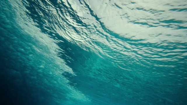 Underwater perspective of powerful ocean wave forming blue curling wall spraying foam and bubbles from vortex, slow motion rearview pan