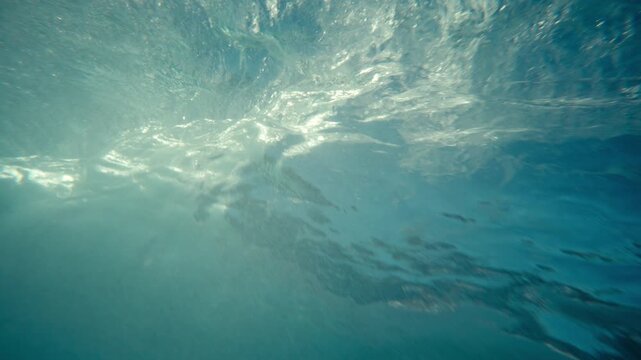 Underwater perspective of large ocean wave forming translucent blue barrel with shimmering dreamy tropical mountains distorted, slow motion