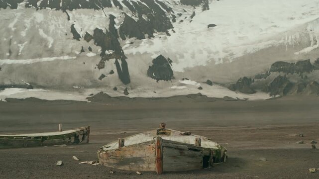 Decaying wooden whaling boats abandoned on dark volcanic ash beach at Whalers Bay Deception Island with snowy mountains behind