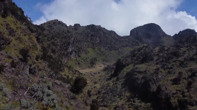 Cinematic drone shot explores the jagged rocky ridges and high-altitude plateaus of Mount Sumbing under a bright midday sun