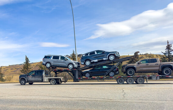 Calgary, Alberta, Canada. April 14, 2026. A heavy-duty car carrier truck transporting several new SUVs and a pickup truck along a highway.