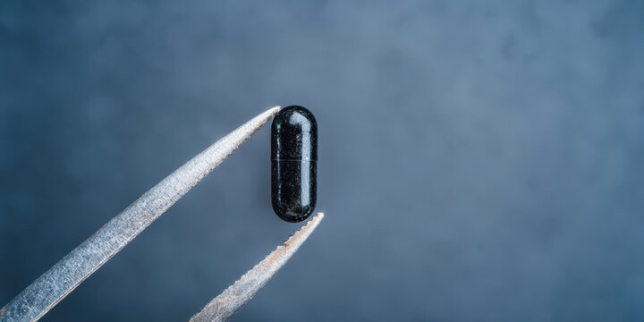 Diagnostic imaging black capsule held by tweezers close up minimal medical still life