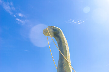 Wooden sauropod dinosaur sculpture with rope halter against bright blue sky with sun flare © Dmitrii