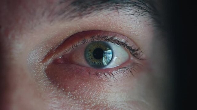 Doomscrolling man eye close up with smartphone news feed reflection in glasses at night. Man scrolling news on phone, endless news feed glowing in eye, digital addiction, information overload
