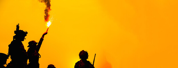 Obraz premium Silhouetted Soldiers Deploy Bright Flare for Tactical Coordination During Intense Desert Training Exercise with Equipment and Teamwork in a Fiery Orange Environment.