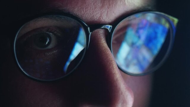 Close up male eyes in glasses reflecting smartphone news feed scrolling rapidly at night. Concept information overload constant online news monitoring, endless search for digital information in media