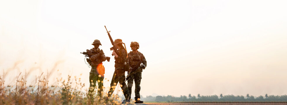 Three Soldiers Conducting Patrol in Rural Field with Rifles, Camouflage Clothing, Serious Expressions, Tactical Equipment Assessment in a Warm-Toned Military Landscape.