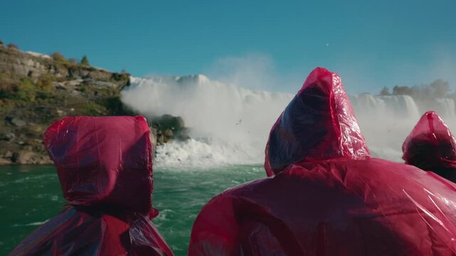 Tourists wearing red rain ponchos watching Niagara Falls waterfall from boat close to the cascade