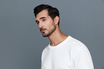 Fototapeta premium Handsome man wearing a white t-shirt looking thoughtfully to the side against a soft grey background, showcasing a contemplative and stylish vibe.