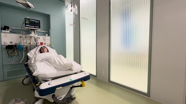 Wide angle view of patient lying in hospital bed with monitoring equipment. Concept for emergency, healthcare, and clinical treatment.