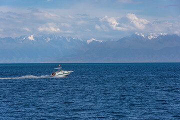 Fototapeta premium Speedboat with red national flag of Kyrgyzstan racing across waves of Issyk-Kul lake