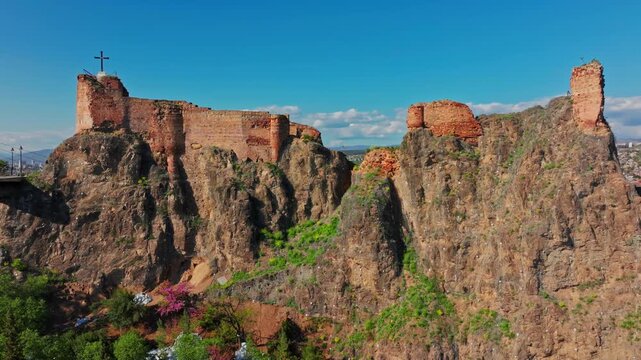 Drone shot of Narikala Fortress, Tbilisi, showing the historic stone stronghold perched above the city with sweeping urban and hillside views.