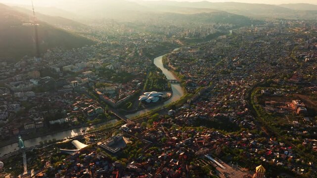 Aerial footage of Tbilisi, Georgia during sunset, showcasing the capital bathed in golden light with layered rooftops and a scenic urban panorama.