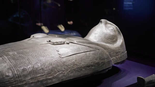 Ancient Egyptian sarcophagus with engraved hieroglyphs displayed in a dimly lit museum exhibition, showcasing detailed craftsmanship and funerary art.