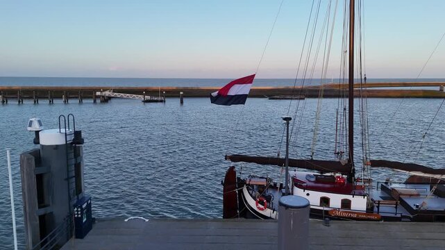 Static harbor detail of ship stern, Dutch flag, mast lines and calm morning sea.