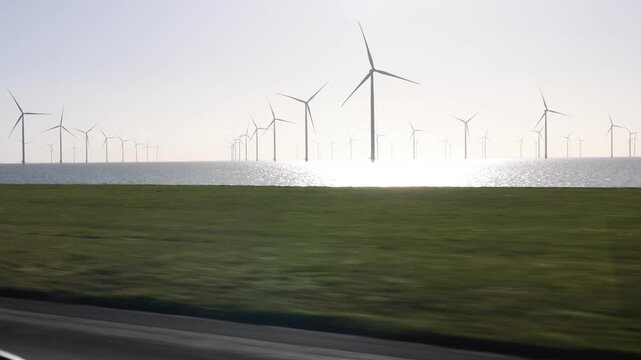 Side perspective across a narrow shoreline with offshore wind turbines under golden morning sun.