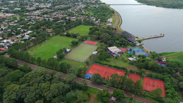 Sports complex with tennis courts soccer field rugby and hockey fields beside Parana River in Posadas, aerial medium dolly