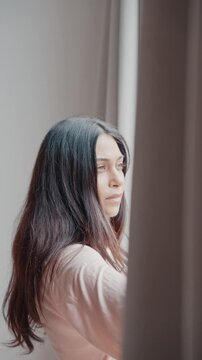 Attractive Young Woman Opening Window Curtains to Let Bright Morning Sunlight Enter Room. Beautiful Girl Looking Outside With Hope. One Adult Female Starting Her Day in Cozy Modern Residence Home 4k