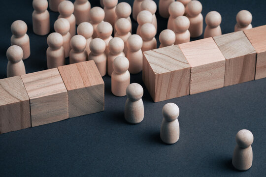 Wooden peg figures face a solid wall made of wooden blocks, representing structural capacity limits, systemic constraints, and organizational barriers in business or institutional environments.