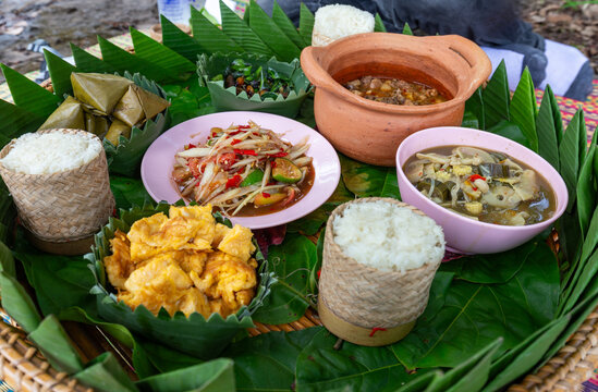 A traditional Northeastern Thai meal served in a Khantoke style includes sticky rice, papaya salad, and mushroom curry.