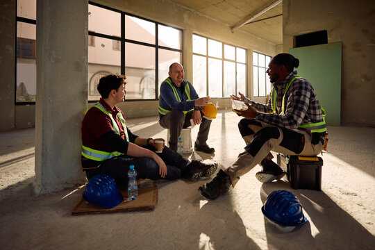 Happy diverse construction workers talking during lunch break on site.