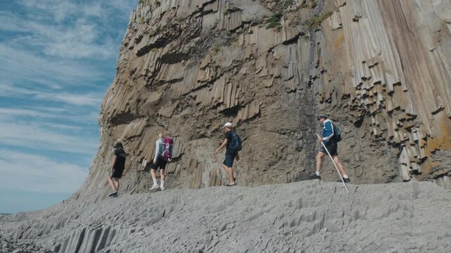 Group of hikers walk on the coast of Kunashir Island near the cape of Stolbchaty with its unique land formations