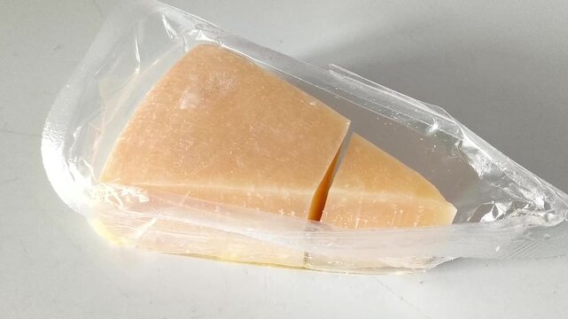 Triangle of hard cheese in a package close-up on a white table. High calcium content in dairy products