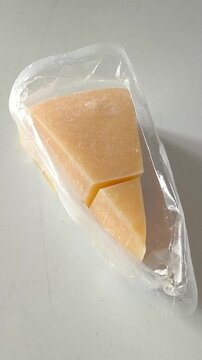 Triangle of hard cheese in a package close-up on a white table. High calcium content in dairy products