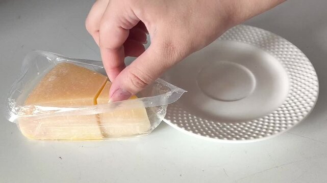 The hand takes a piece of cheese from the package and puts it in a plate. Hard cheeses with a high calcium content