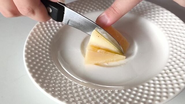 The hand uses a knife to cut the triangle of cheese in the plate. Hard cheeses. Calcium, potassium in lactic acid products