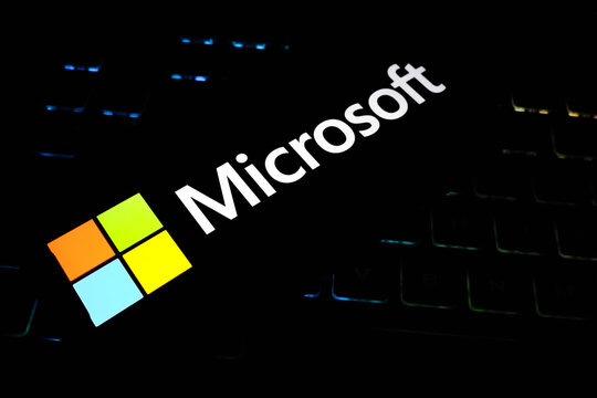 Colorful Microsoft Logo and Wordmark Glowing Against a Dark Backlit Mechanical Gaming Keyboard Background - Concept for Modern Computing, Software Innovation, and Global Tech Branding