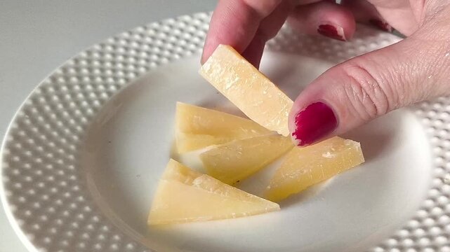 The hand takes a piece of cheese from the plate. Hard cheese in a woman's hand close-up. Calcium, potassium in products