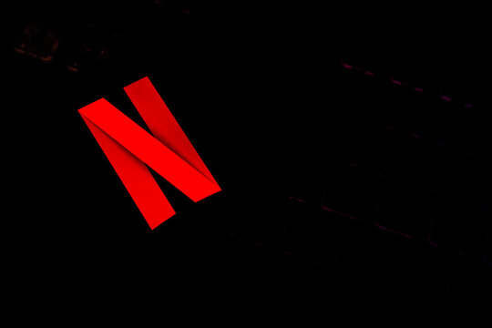 Vibrant Red Netflix "N" Logo Glowing on a Smartphone Screen Over a Dark Backlit Gaming Keyboard Background - Concept for Online Video Streaming, Digital Entertainment, and Modern Tech Trends